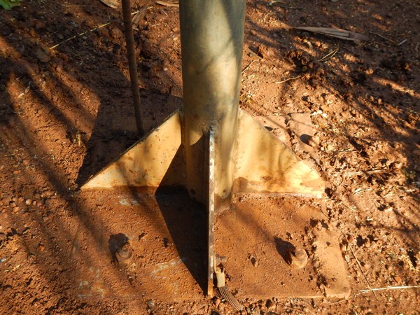 The steel base plate of a lightning conductor mast, bolted down in red soil